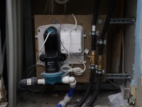 In der Wand wird hinter einer fliesengroßen Revisions-Öffnung die Membran-Pumpe angebracht. Sie ist zur Schallentkopplung auf einer Platte angebracht. Die Pumpe ist mit einer dünnen Abflussleitung (Durchmesser 22 mm) mit dem Duschboard verbunden.