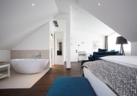 Im diesem Hotelzimmer steht die Badewanne frei im Raum – großformatige Fliesen an Wand und Boden trennen den Bereich optisch vom restlichen Raum ab.