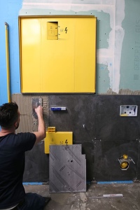 Während der Beplankung und anschließenden Befliesung mit den großflächigen, anthrazitfarbenen Fliesen sind Spiegelschrank und Revisionsöffnung der Funktionsbox mit einem Bauschutz abgedeckt.